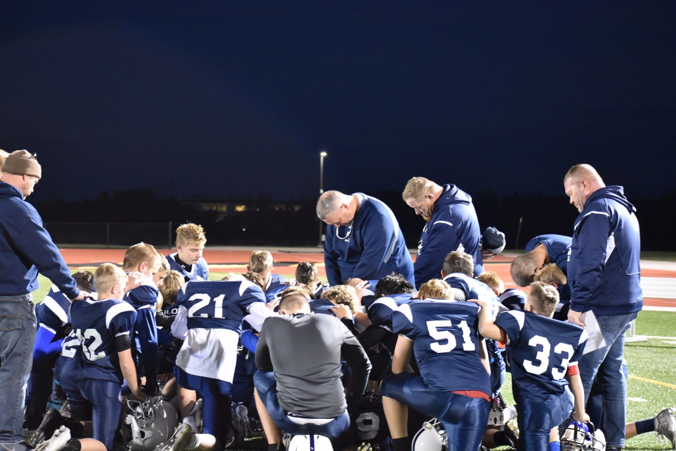 Coaches and players in a team huddle at dusk